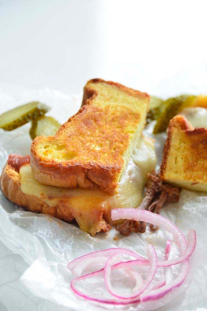 3 cheese keto grilled cheese sandwich on parchment paper with pickles and red onions