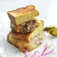 3 cheese keto grilled cheese sandwich on parchment paper with pickles and red onions