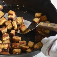 bacon croutons in a cast iron skillet with a wood handled spatula