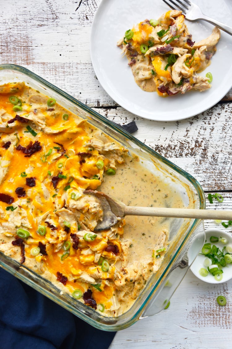 baked crack chicken in a glass casserole dish with a wooden spoon and scallions