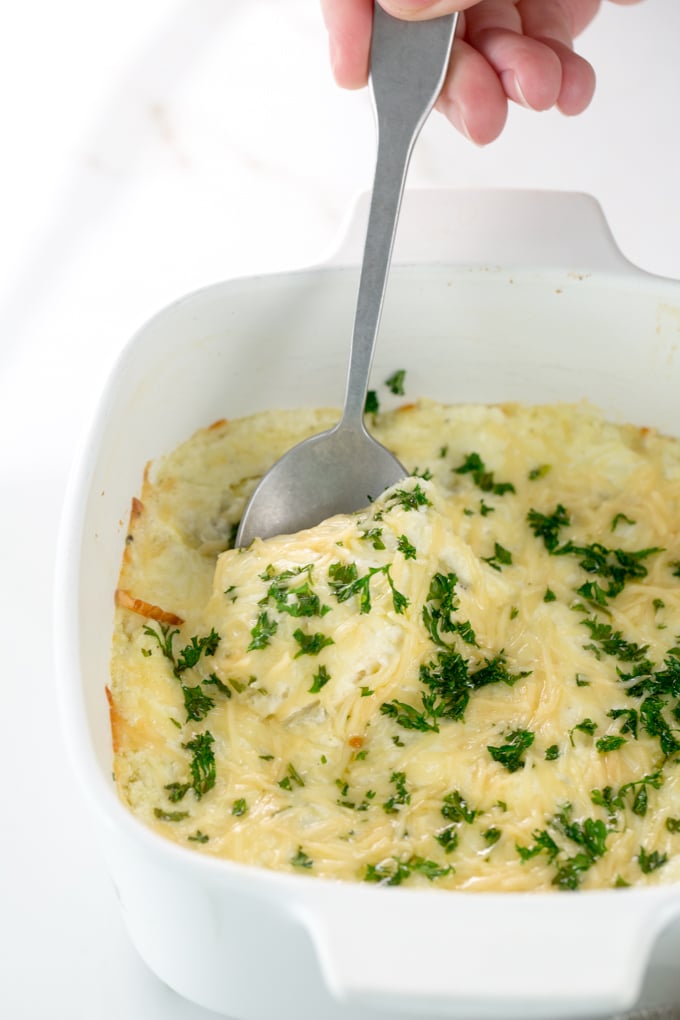 Vertical image of Baked Creamy garlic parmesan hot artichoke dip in a white square casserole dish with a silver spoon