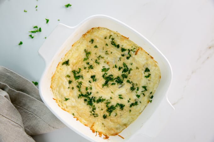 square image of Baked Creamy garlic parmesan hot artichoke dip in a white square casserole dish
