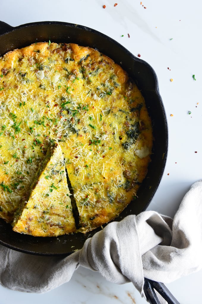 vertical image of a baked frittata in a cast iron skillet close up with a white fabric napkin