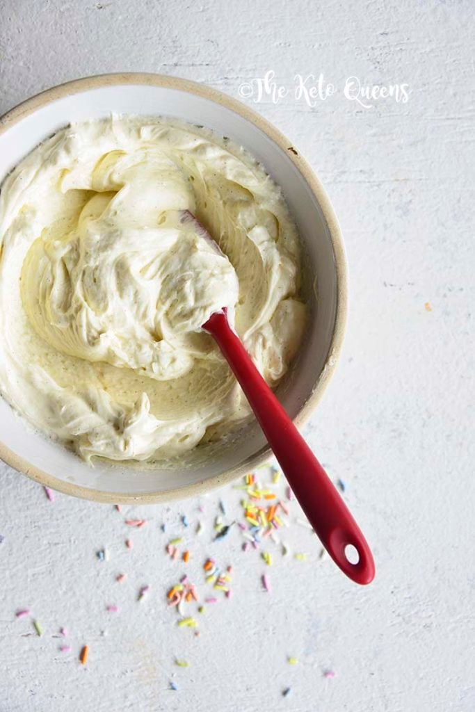 vertical overhead image of white chocolate buttercream icing with a red utensil in it