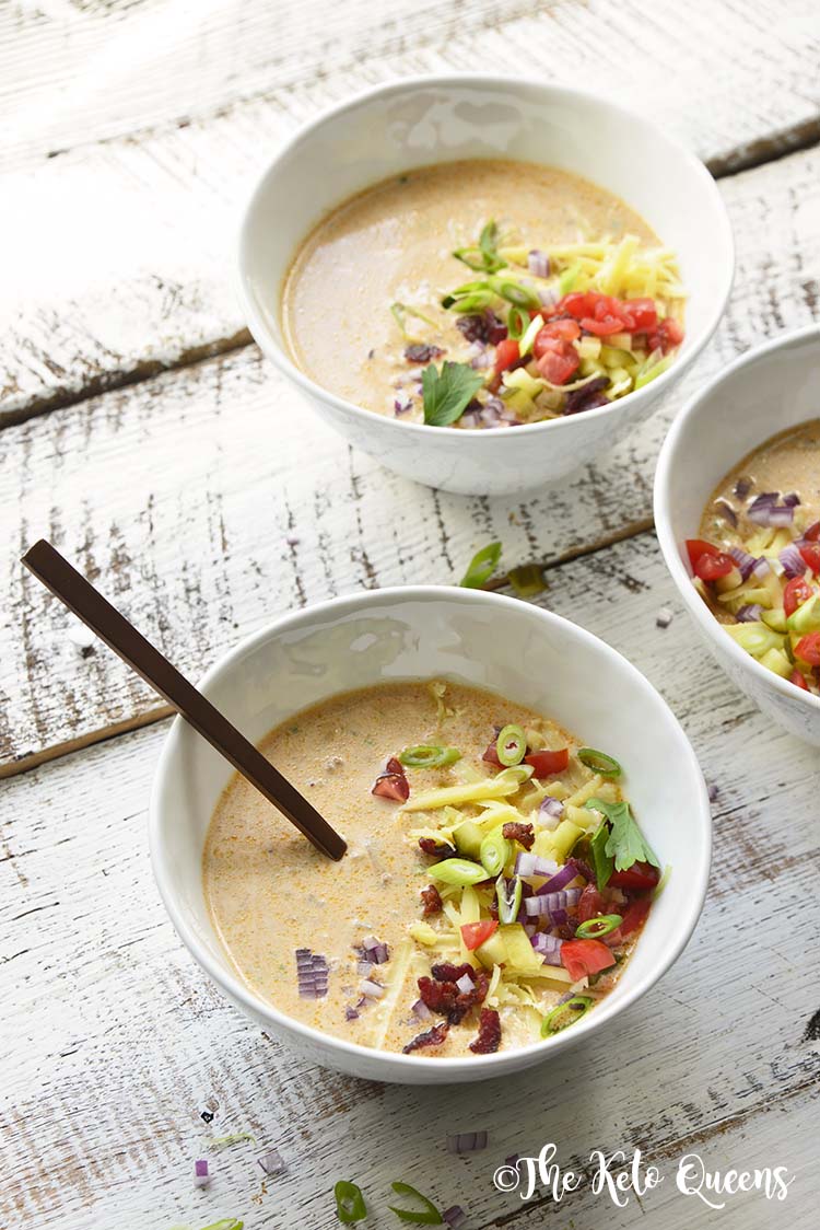 3 bowls of Keto Bacon Cheeseburger Soup with garnishes and a spoon on a white wooden background