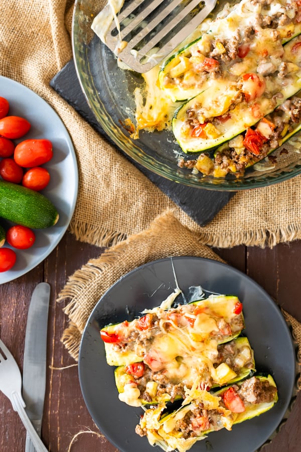 slow cooker BBQ brisket stuffed zucchini boats on dark plates with a side of tomatoes