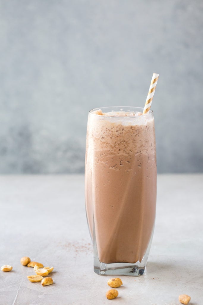 low carb chocolate peanut butter milkshake in a tall glass with a straw on a grey background