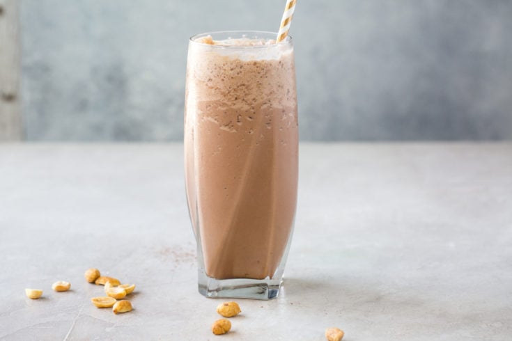 low carb chocolate peanut butter milkshake in a tall glass with a straw on a grey background