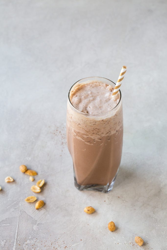 low carb chocolate peanut butter milkshake in a tall glass with a straw on a grey background