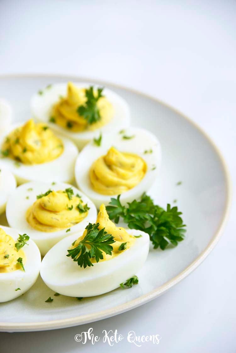 Vertical Image of a bunch of keto Instant Pot Deviled Eggs with Relish on a white plate with a white background with parsley on top