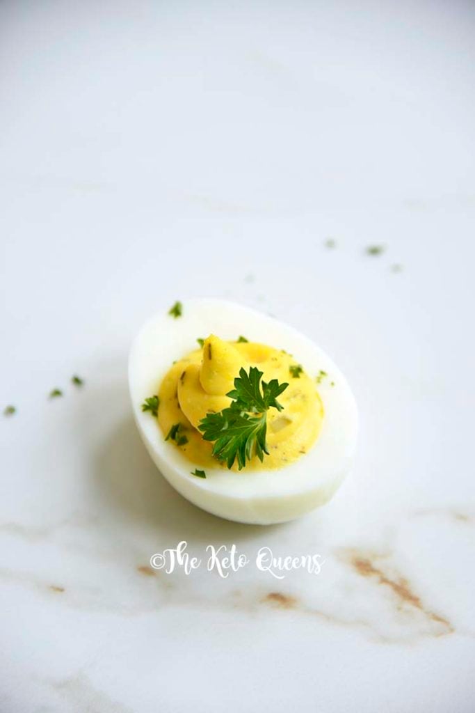 Vertical Image of 1 keto Instant Pot Deviled Eggs with Relish on a white plate with a white background with parsley on top