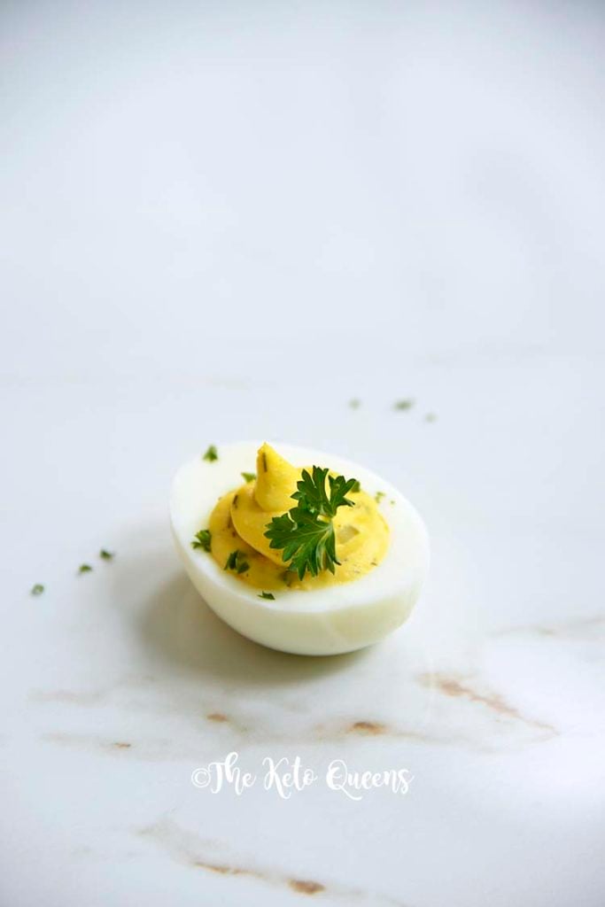 Vertical Image of 1 keto Instant Pot Deviled Eggs with Relish on a white plate with a white background with parsley on top