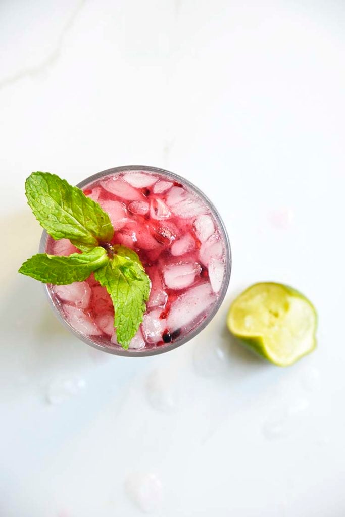 Sparkling Blackberry Bourbon Smash in a clear class topped with mint and lemon wedge on the side