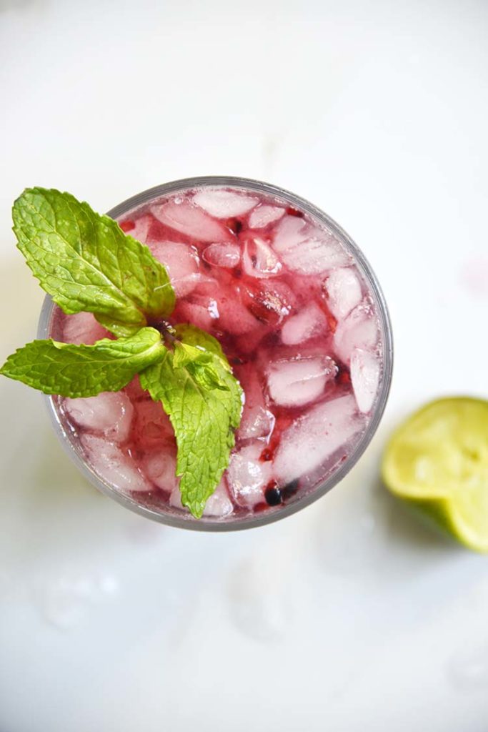 Sparkling Blackberry Bourbon Smash in a clear class topped with mint and lemon wedge on the side