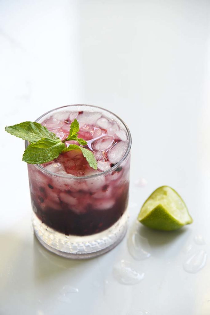 Sparkling Blackberry Bourbon Smash in a clear class topped with mint and lemon wedge on the side