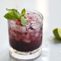 Sparkling Blackberry Bourbon Smash in a clear class topped with mint and lemon wedge on the side