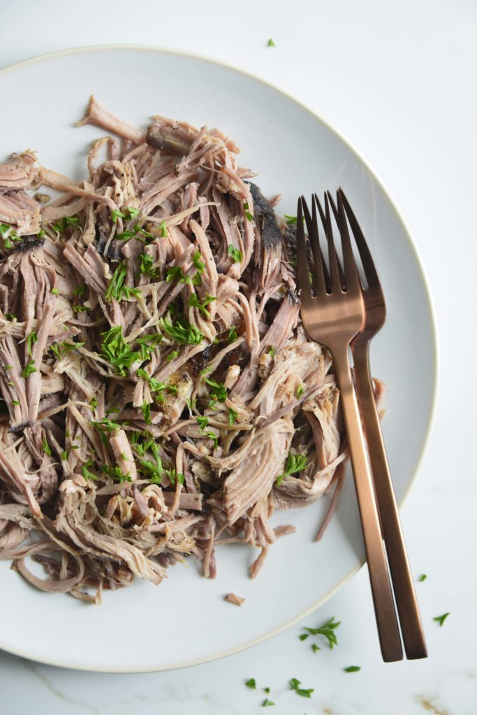 slow cooker pork butt shredded on a white plate with 2 forks
