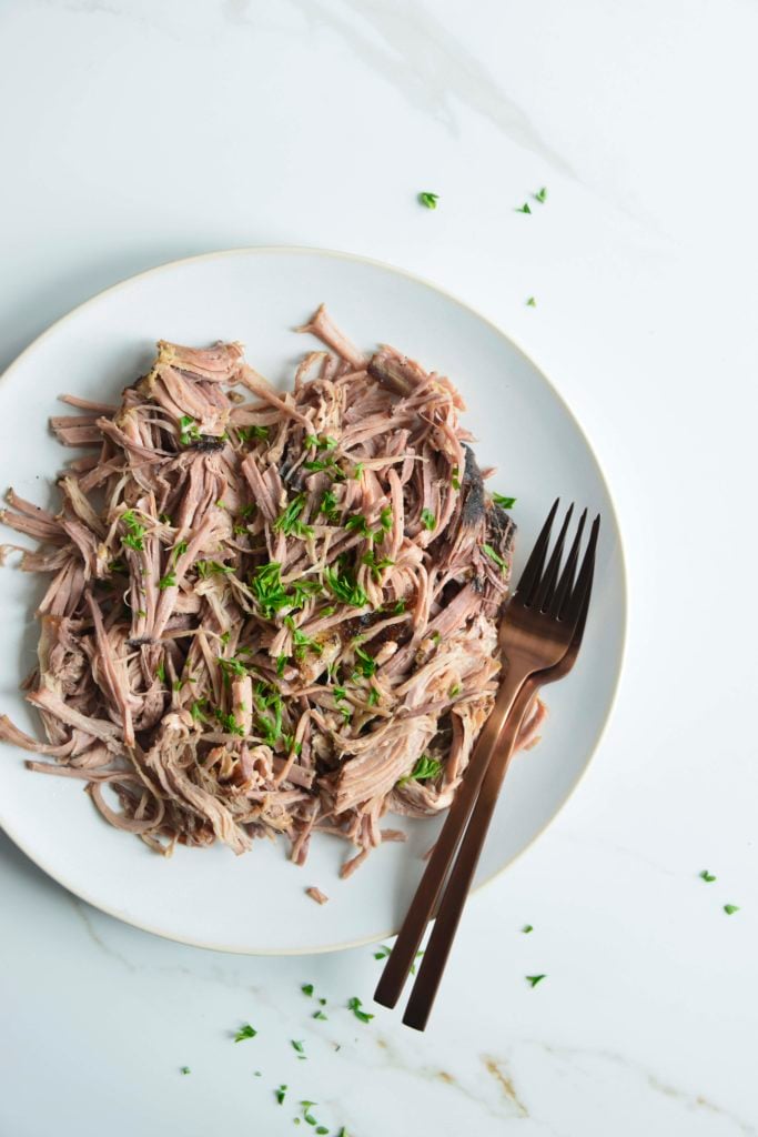 slow cooker pork butt shredded on a white plate with 2 forks
