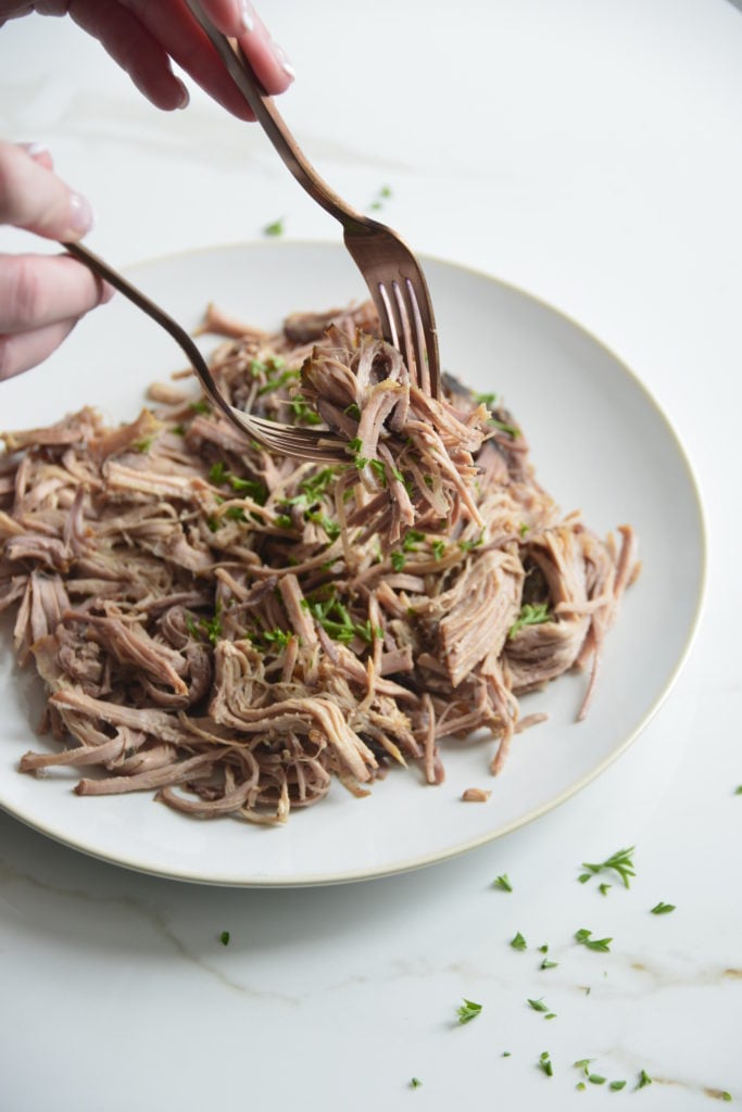 slow cooker pork butt being shredded with 2 forks