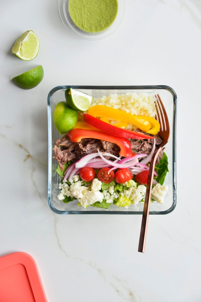 Prepared keto chipotle bowls in square glass meal prep containers with sliced limes and a fork