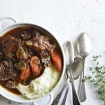 vertical image of low carb instant pot beef stew in a white bowl with 3 spoons and fresh herbs on a white background