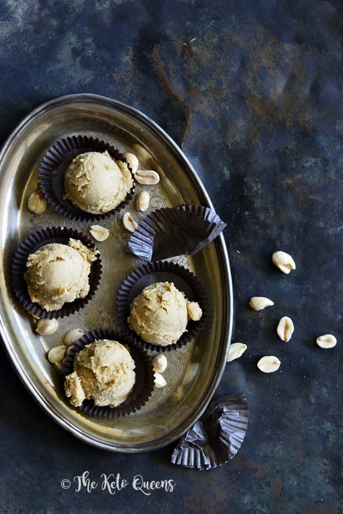 vertical image of keto breakfast meal prep of Keto Peanut Butter Cookie Dough Fat Bombs on a silver platter with black wrappers with peanuts sprinkled everywhere