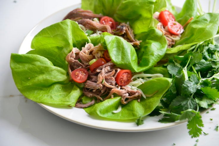 Lettuce Wrapped Leftover Pulled Pork Tacos topped with cheese and tomatoes on a white plate