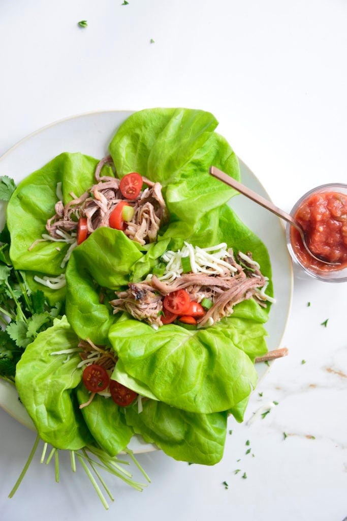 Lettuce Wrapped Leftover Pulled Pork Tacos topped with cheese and tomatoes on a white plate