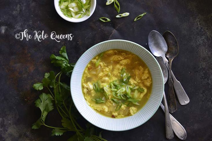 Horizontal picture of egg drop soup over head shot with scallions and spoons on a dark surface