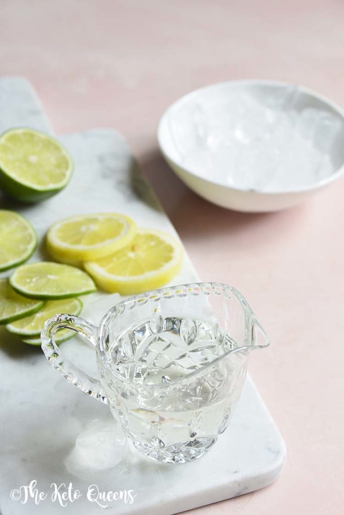 keto lemonade ingredients on a white slate with slices of lemon on a pink background