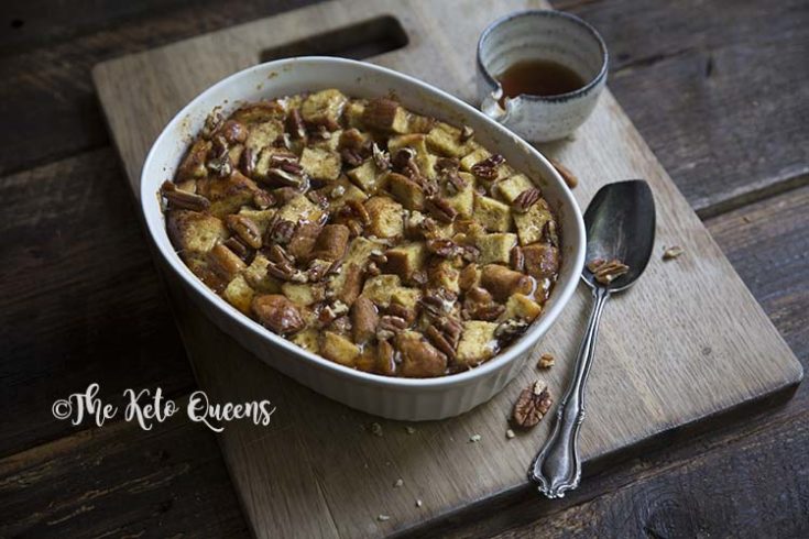 zoomed out horizontal image of maple pecan french toast casserole in a white casserole dish, with a spoon and low carb syrup on a wood background