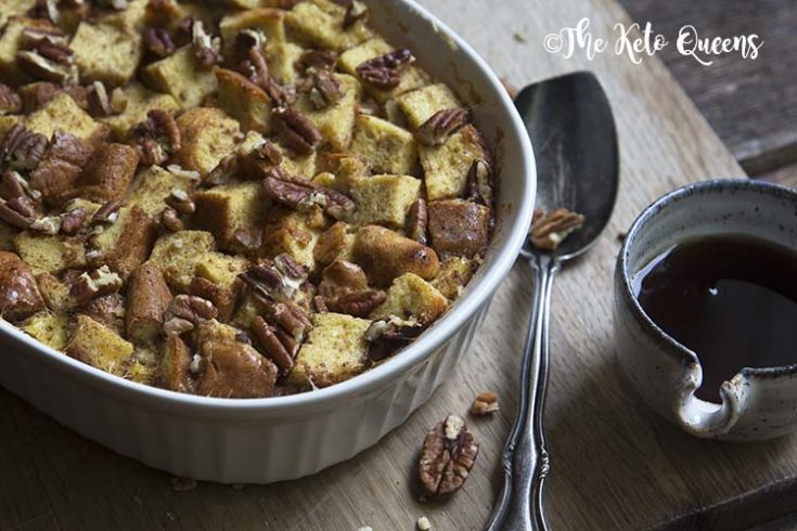 horizontal image of maple pecan french toast casserole in a white casserole dish, with a spoon and low carb syrup on a wood background