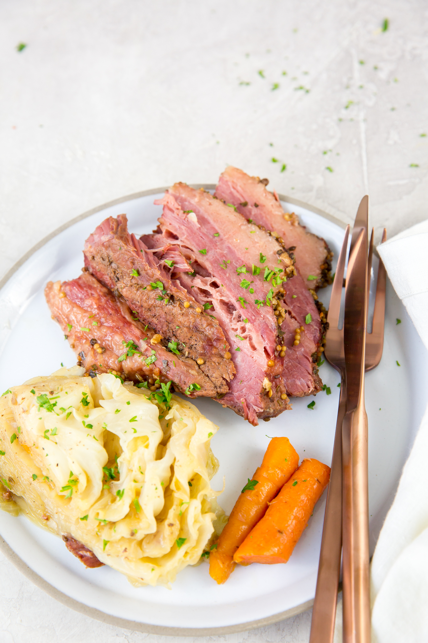 pressure cooker corned beef and cabbage vertical image of corned beef, cabbage and carrots on a white plate with rose-colored fork and knee with napkin and parsley