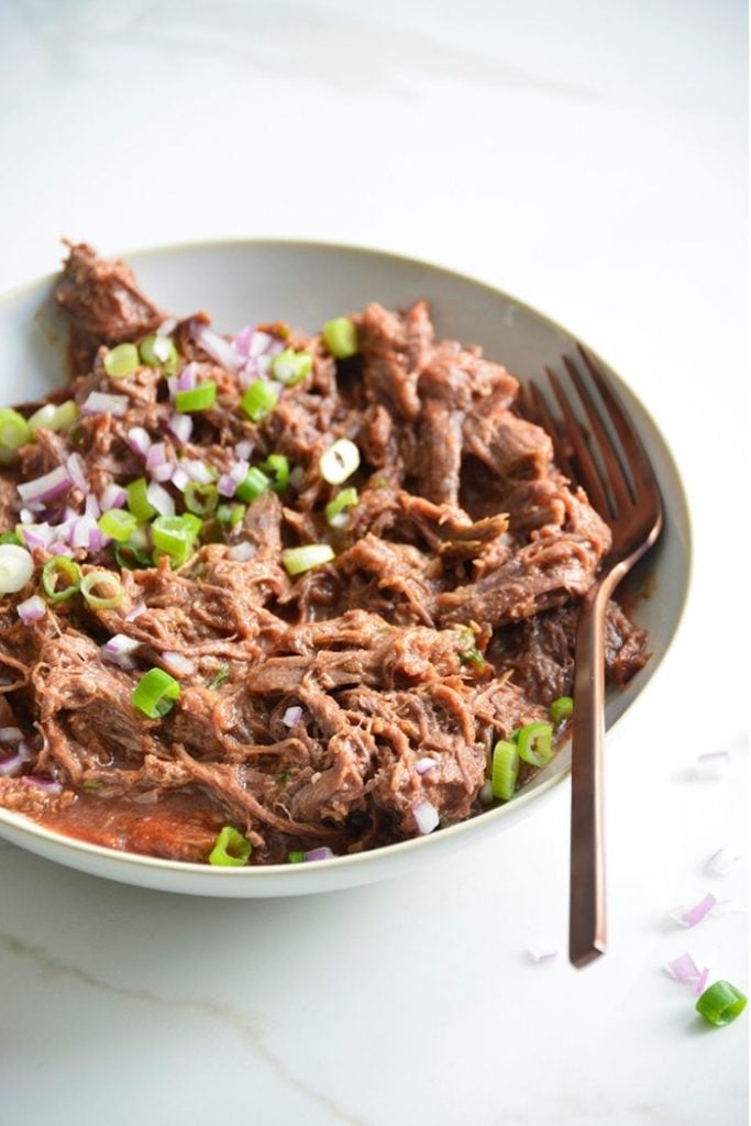 low carb pulled bbq beef recipe in a bowl with a fork on a white background