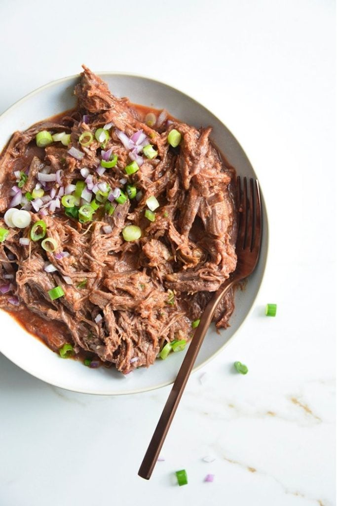 low carb pulled bbq beef recipe in a bowl with a fork on a white background