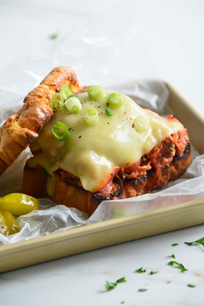 Keto BBQ Pulled Pork Sandwich on parchment paper with scallions and pickles