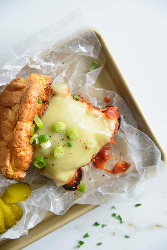 Keto BBQ Pulled Pork Sandwich on parchment paper with scallions and pickles