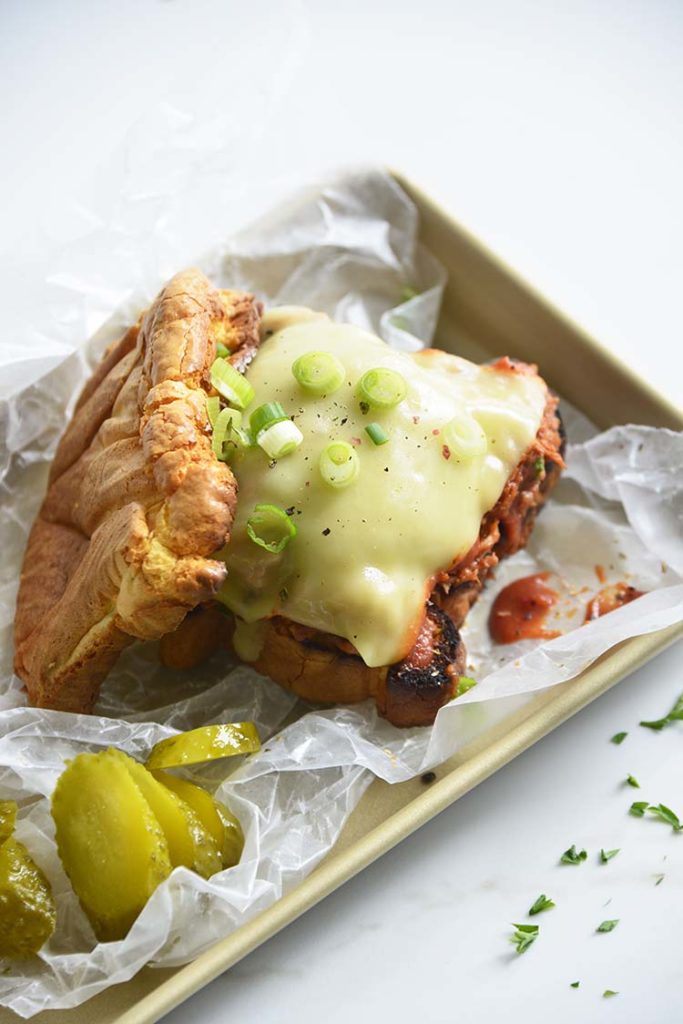 Keto BBQ Pulled Pork Sandwich on parchment paper with scallions and pickles