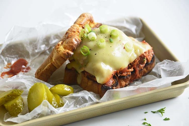 Keto BBQ Pulled Pork Sandwich on parchment paper with scallions and pickles