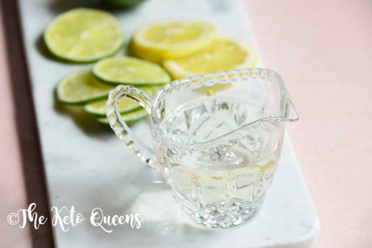 keto simple syrup in a glass with lemons and limes on a marble slate