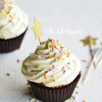 vertical image of a keto vanilla cupcake with white chocolate buttercream frosting with sprinkles and a star