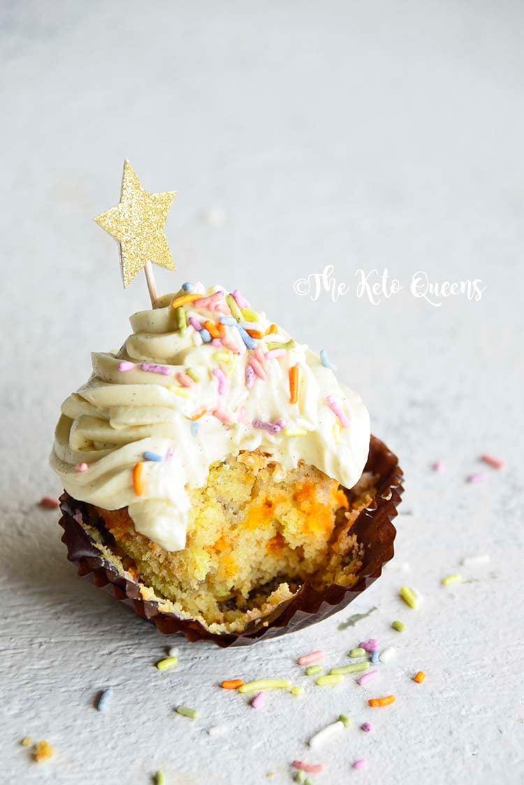 vertical image of a keto vanilla cupcake with white chocolate buttercream frosting with sprinkles and a star with a bite taken out of it