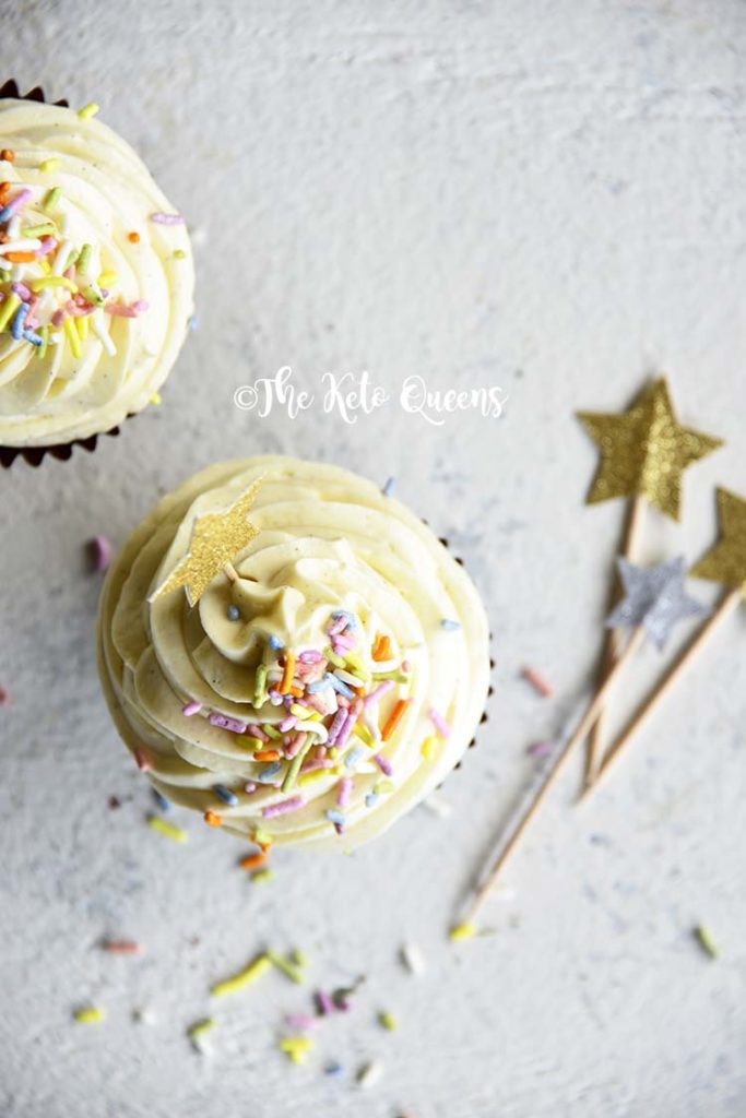 vertical overhead image of a keto cupcake - vanilla cupcake with white chocolate buttercream frosting with sprinkles and a star