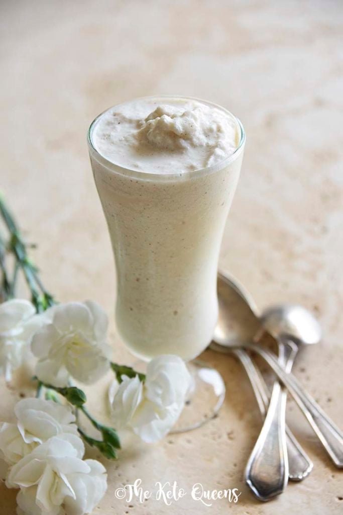 homemade vanilla bean keto milkshake in a tall glass with spoons and white flowers