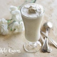 homemade vanilla bean keto milkshake in a tall glass with spoons and white flowers